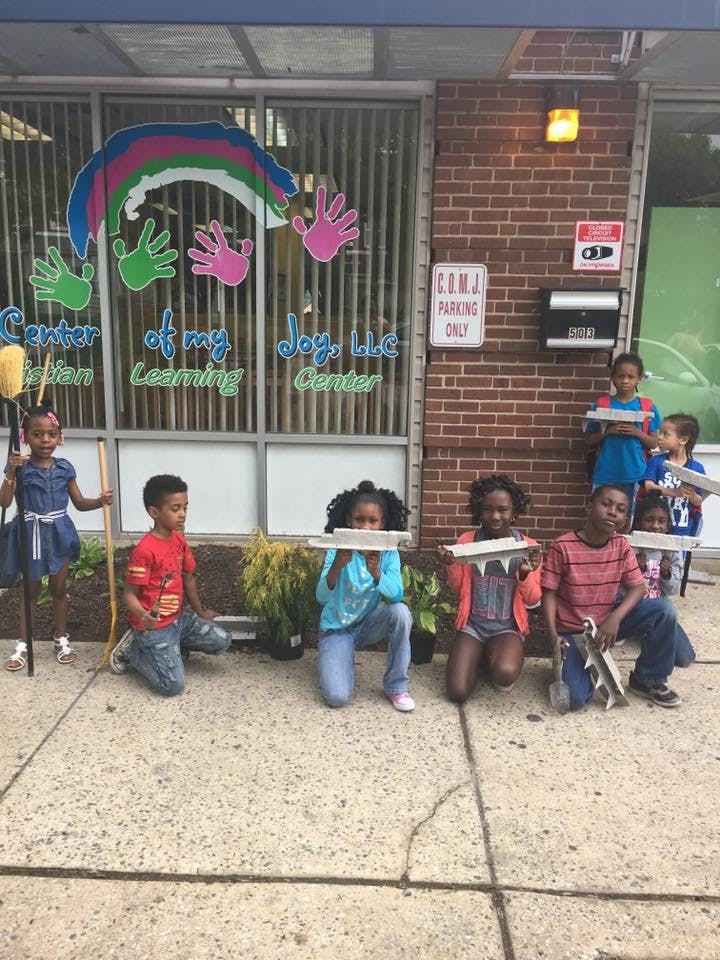 Children holding wooden planks and brooms outside a building