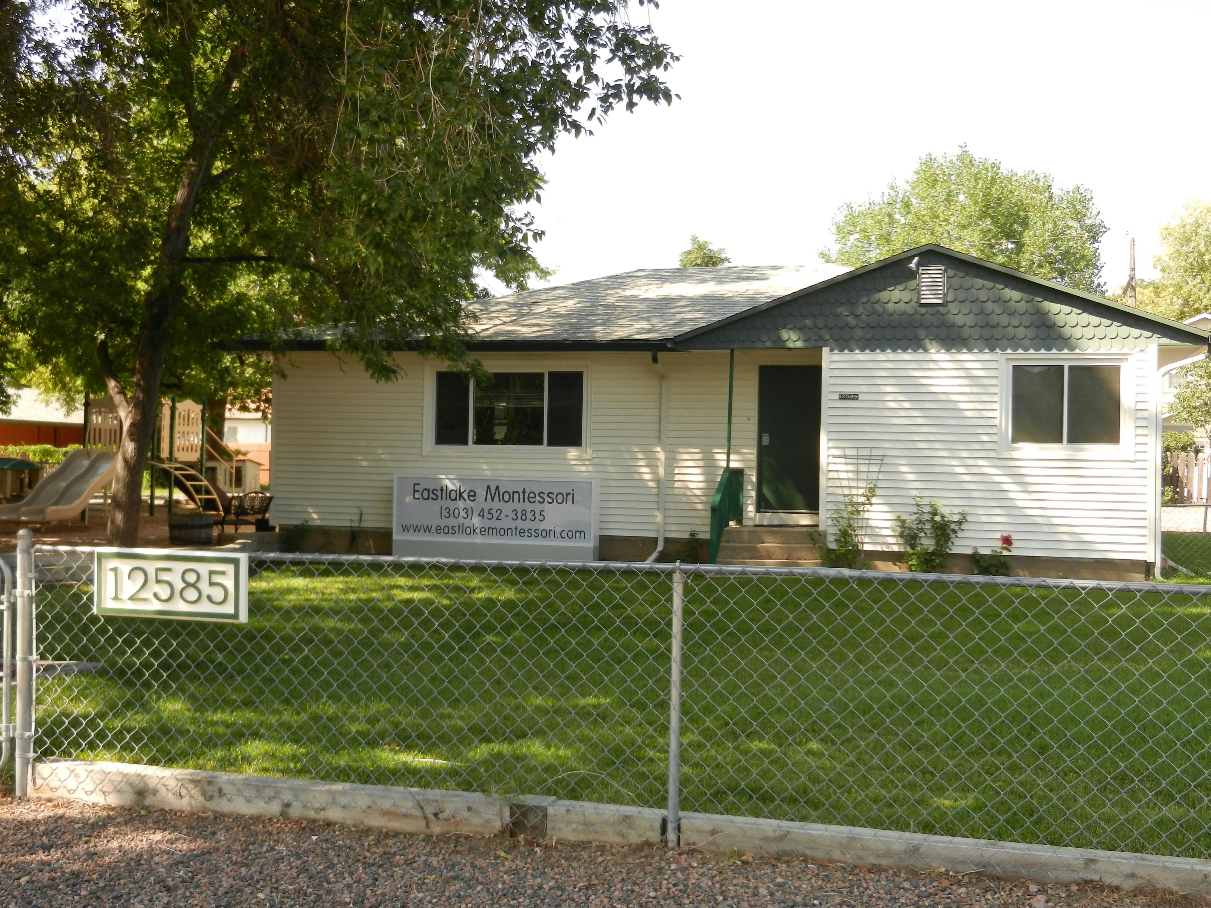 White house with dark green roof and a chain link fence in front