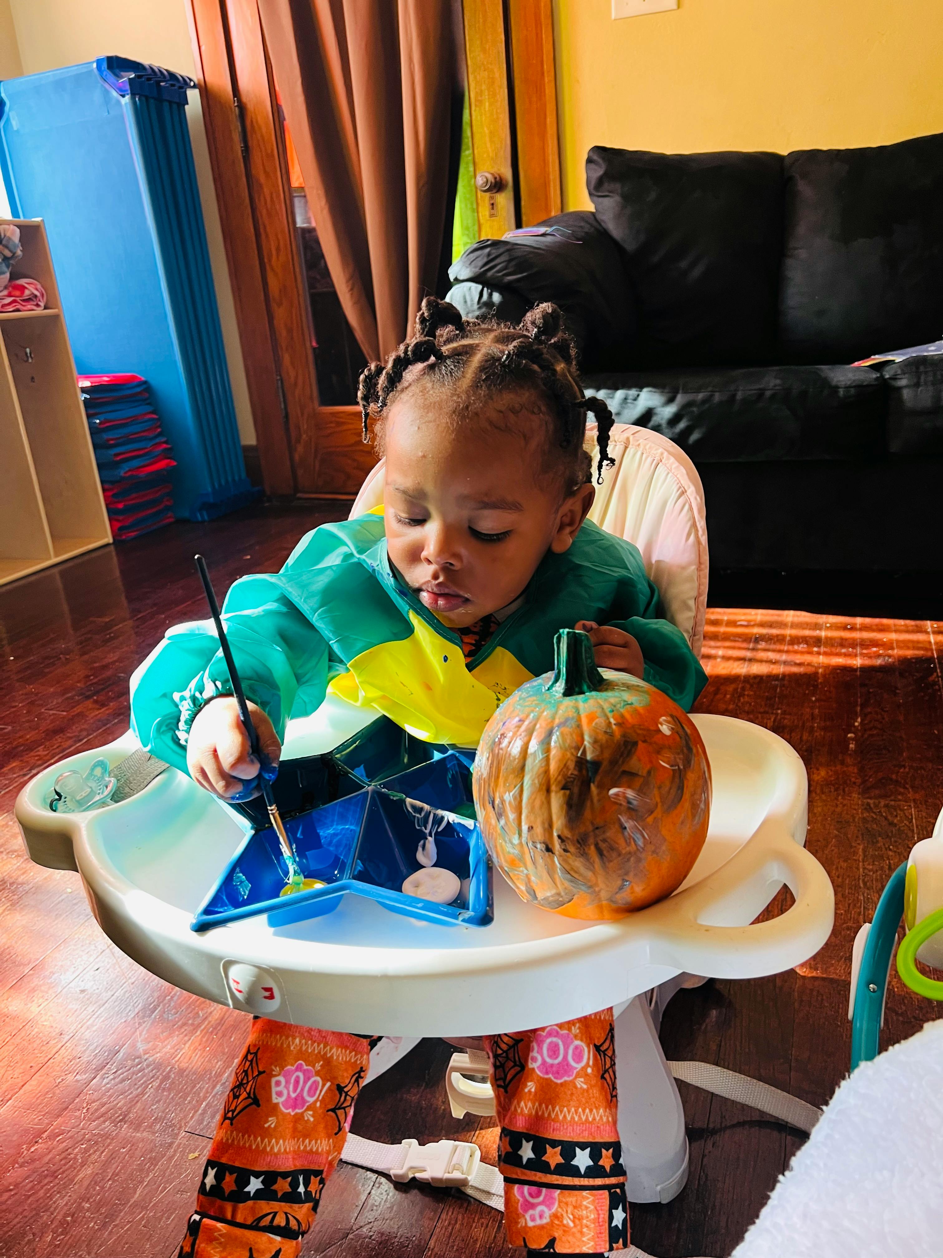 Child painting a pumpkin in a high chair