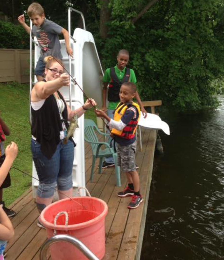 Person holding a fish on a fishing line with children on a dock