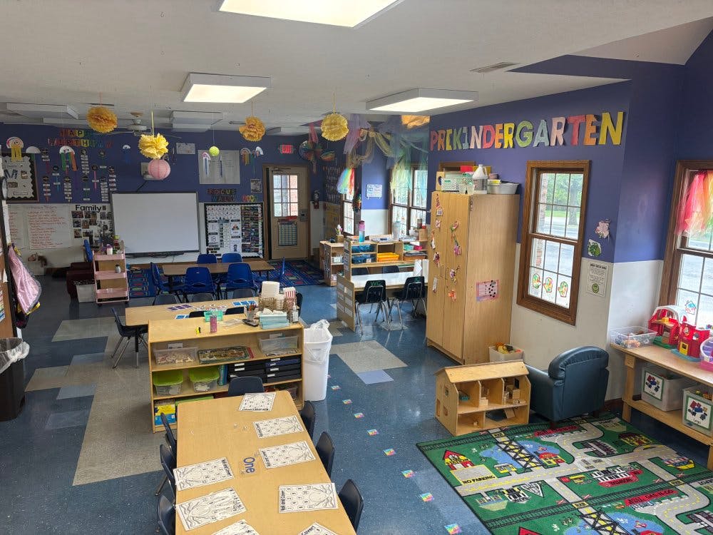 Colorful classroom with tables, chairs, and shelves, sign reads "Prekindergarten"