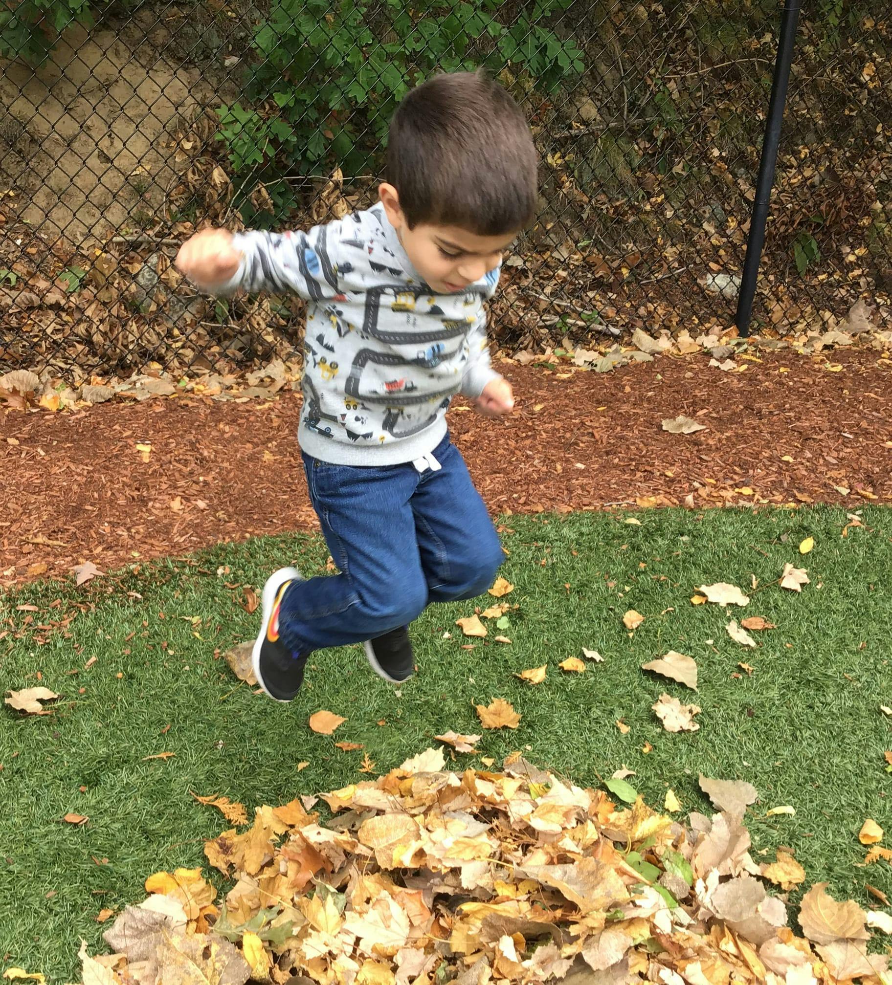 Child jumping over a pile of leaves
