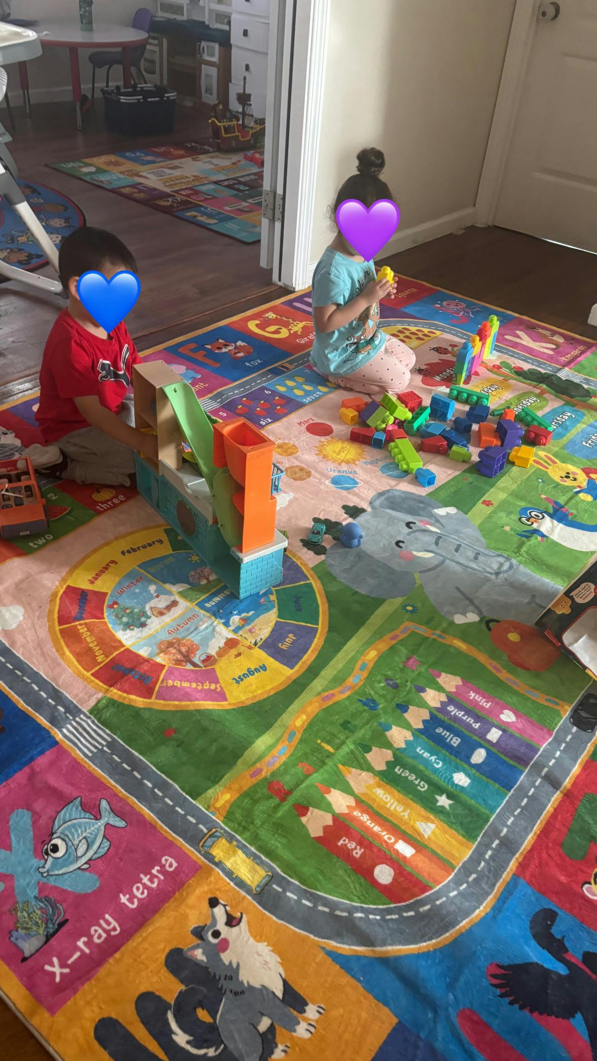 Two children playing on a colorful learning mat with building blocks and toys
