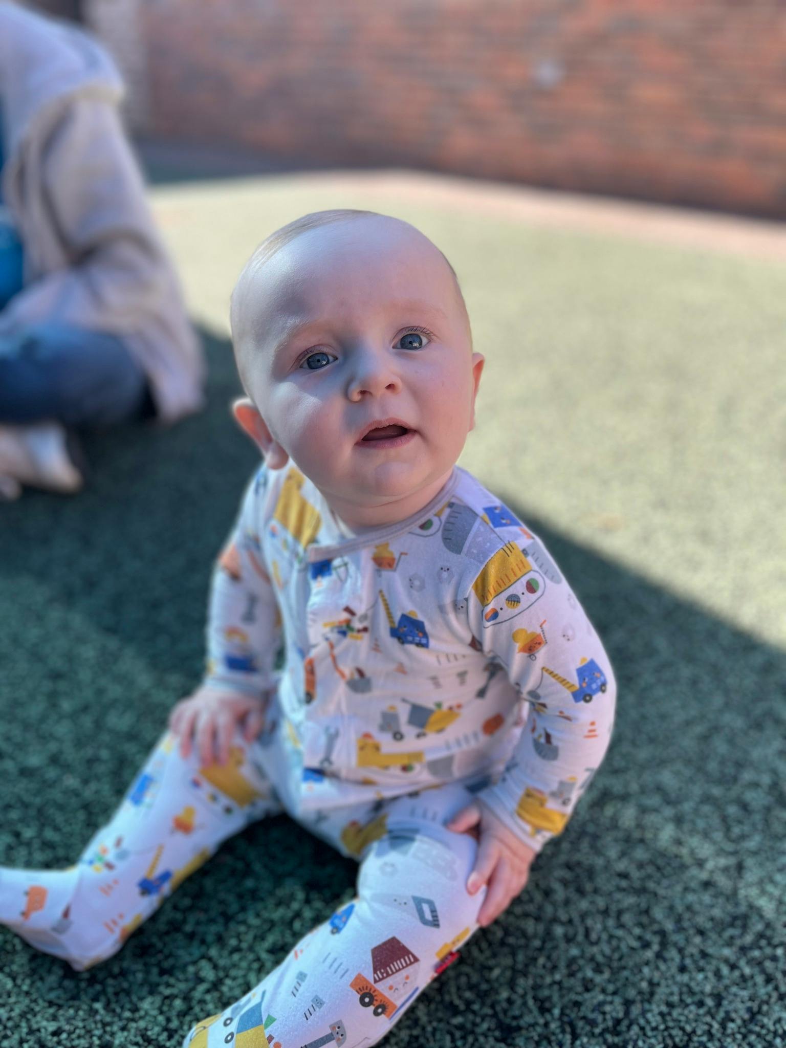 Child in a patterned onesie sitting on the ground