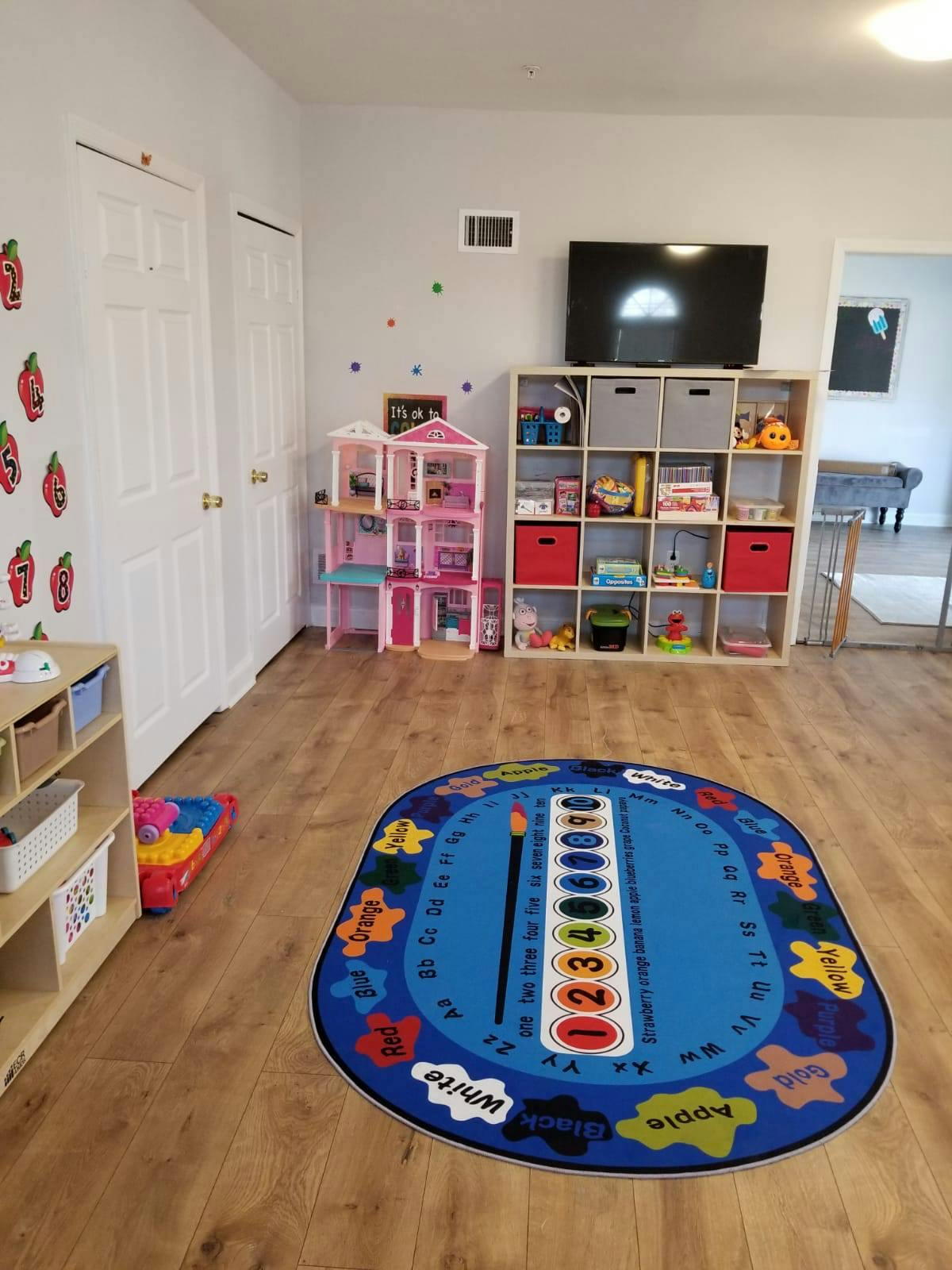 Playroom with a blue rug, dollhouse, and shelves