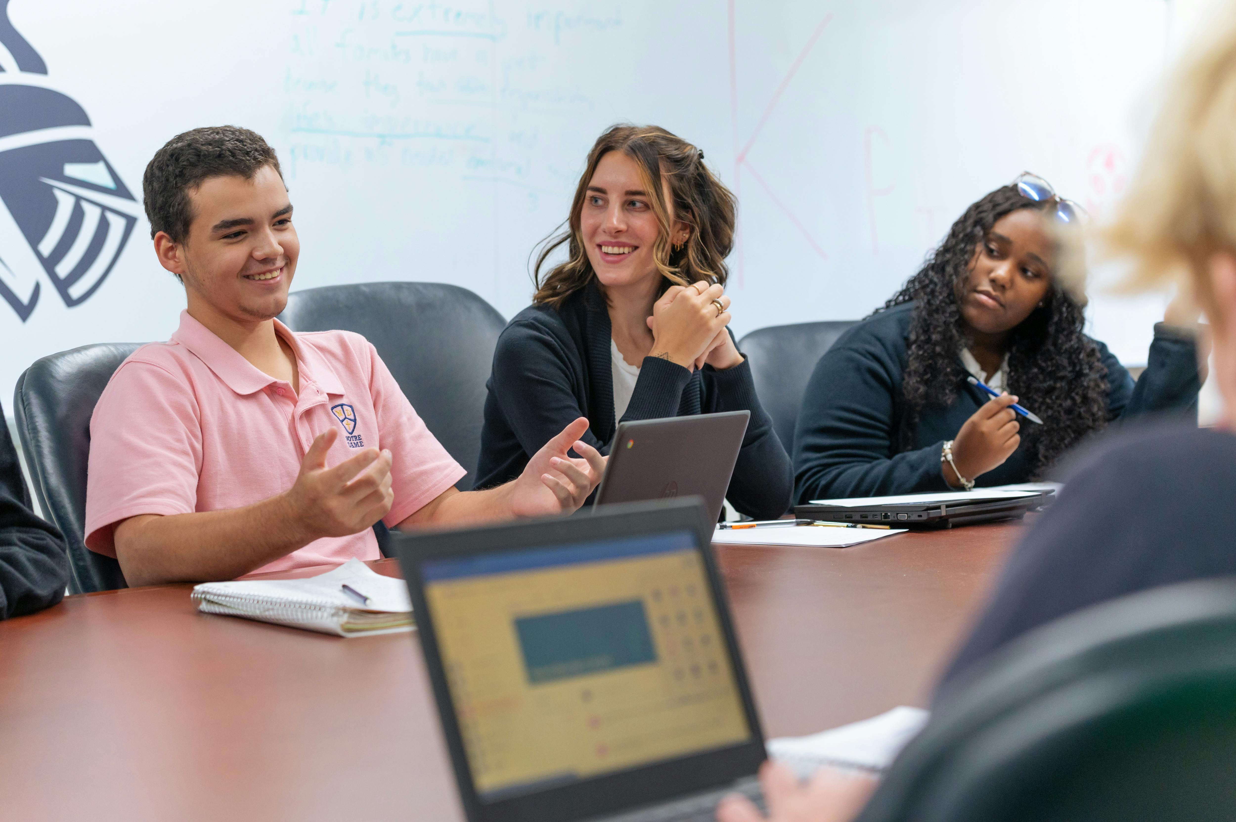 Three people sitting at a table with laptops and notebooks