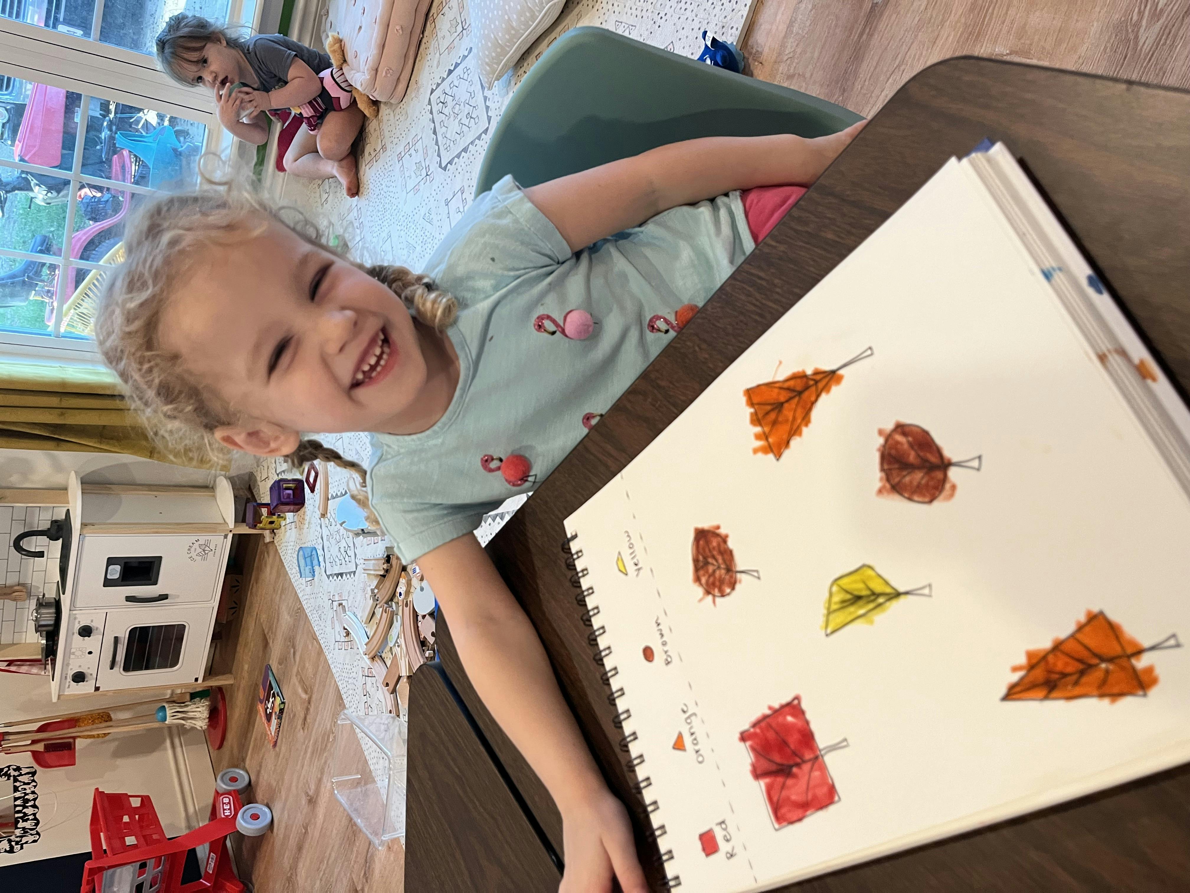 Child smiling at a table with a book open to illustrations of leaves