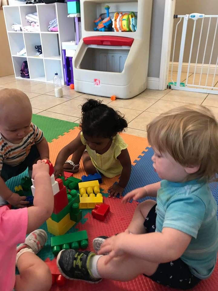 Three children playing with colorful building blocks on a mat