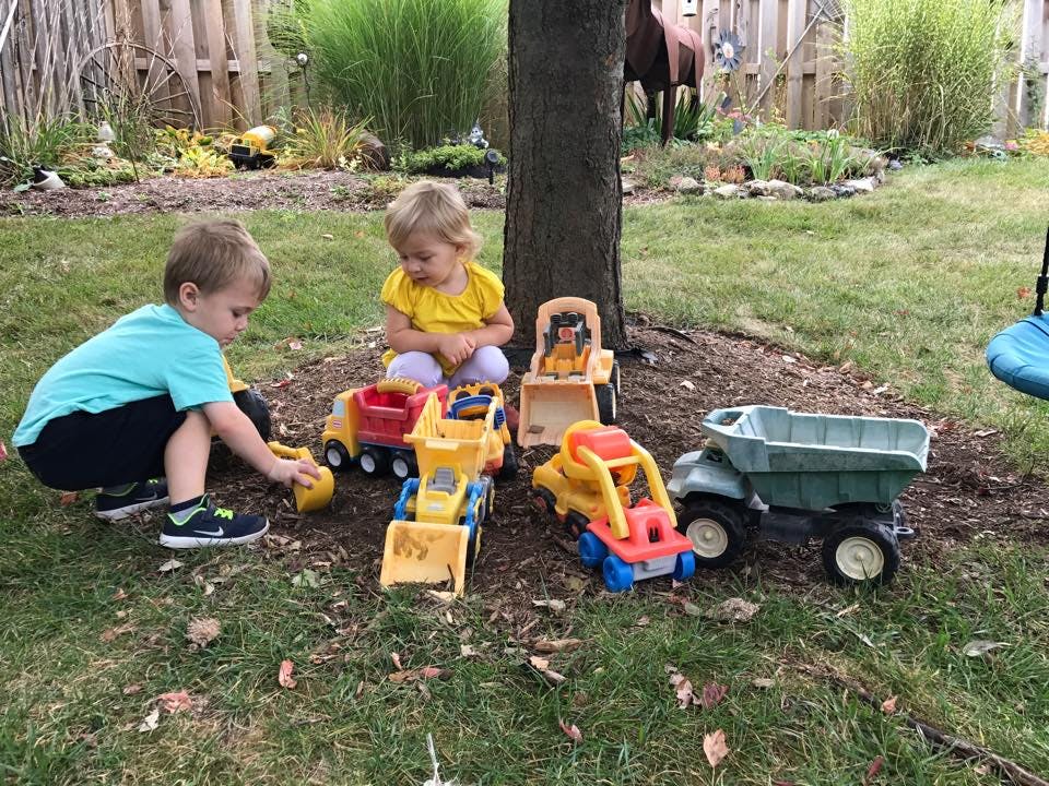 Two children playing with toy construction vehicles outdoors