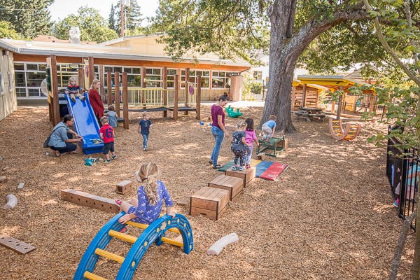 People and children playing on a playground with slides and climbing structures