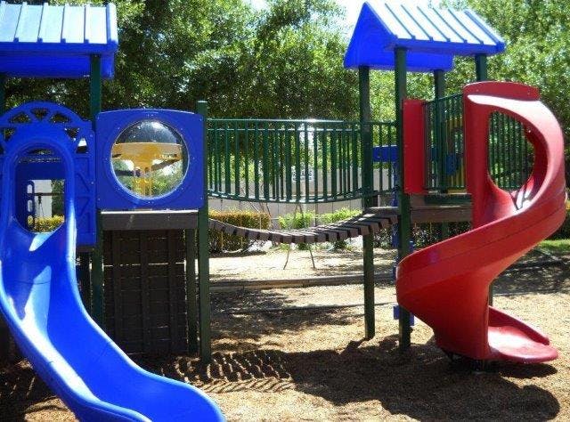 Playground with blue and red slides and a rope bridge