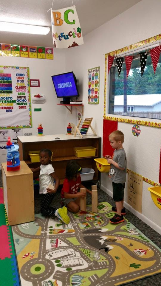 Three children playing with blocks on a road map rug in a classroom