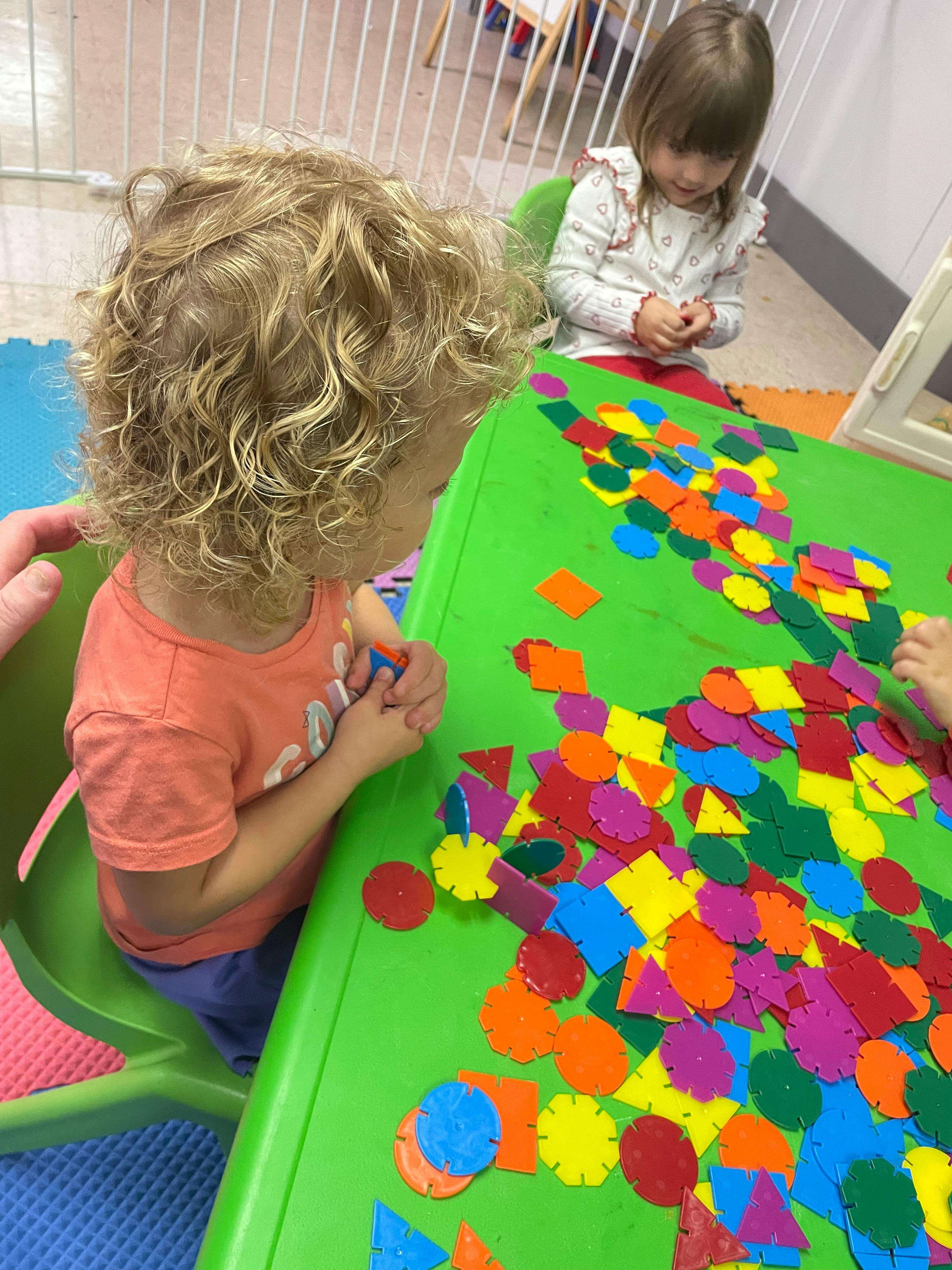 Two children playing with colorful shape cutouts on a green table