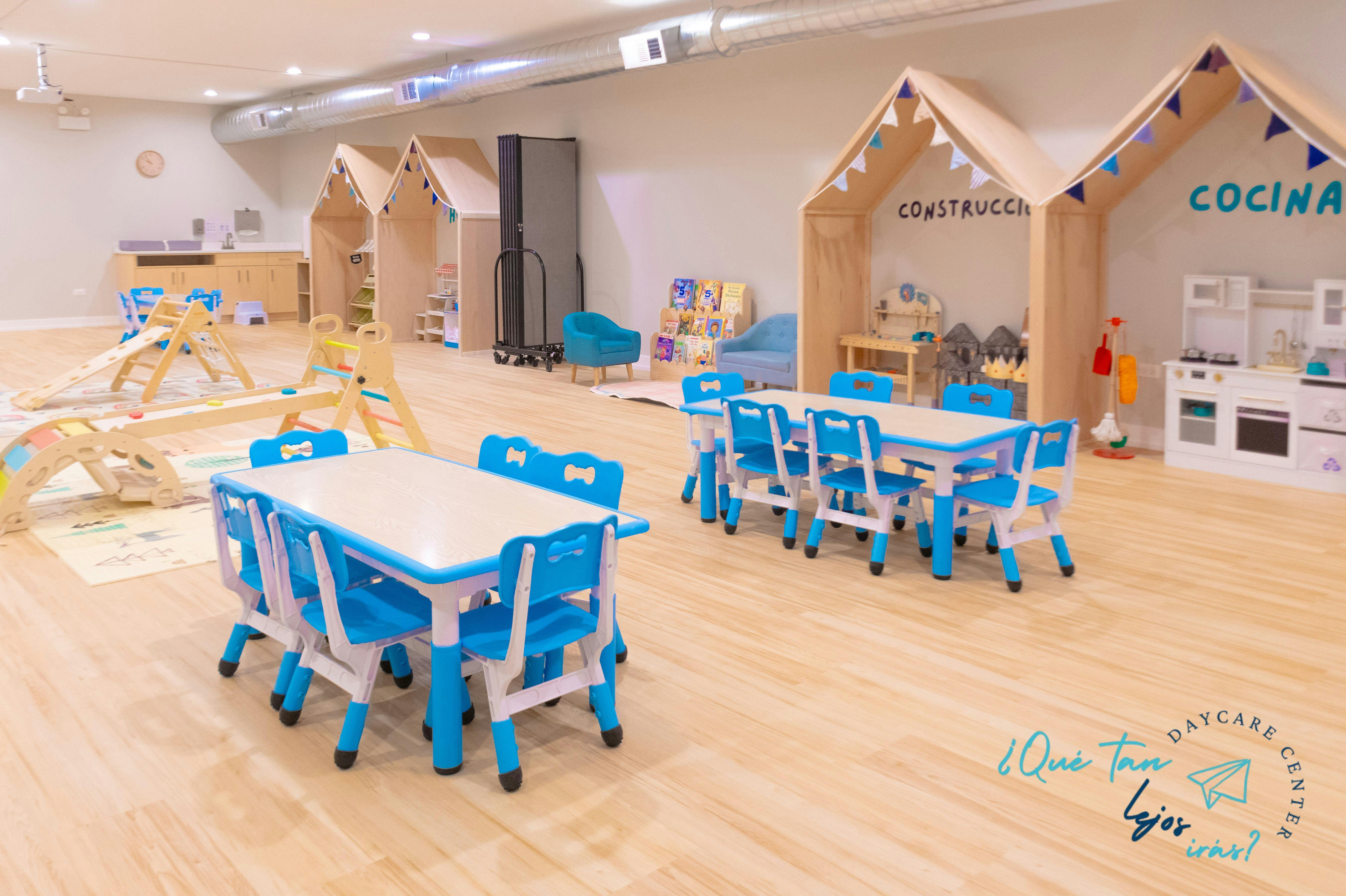 Classroom with child-sized tables and chairs, play structures, and small house play areas