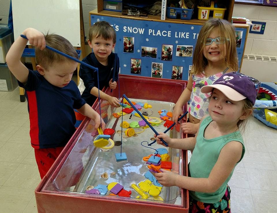 Four children playing with fishing toys in a water table
