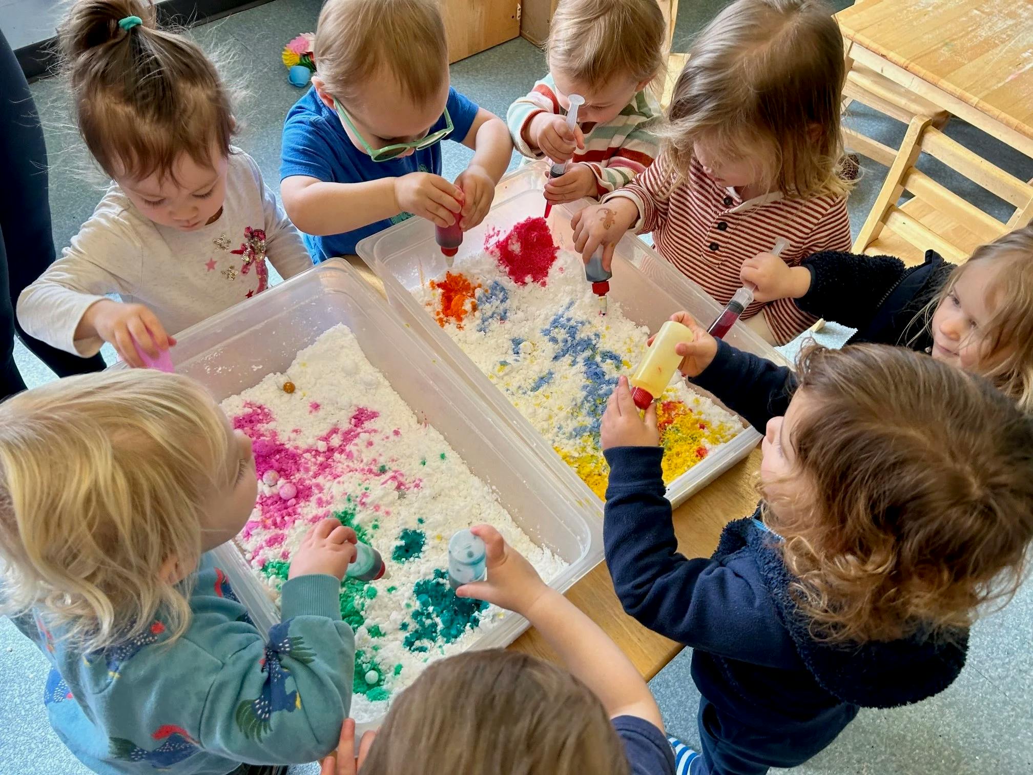 Children playing with colored powders and liquids in plastic bins