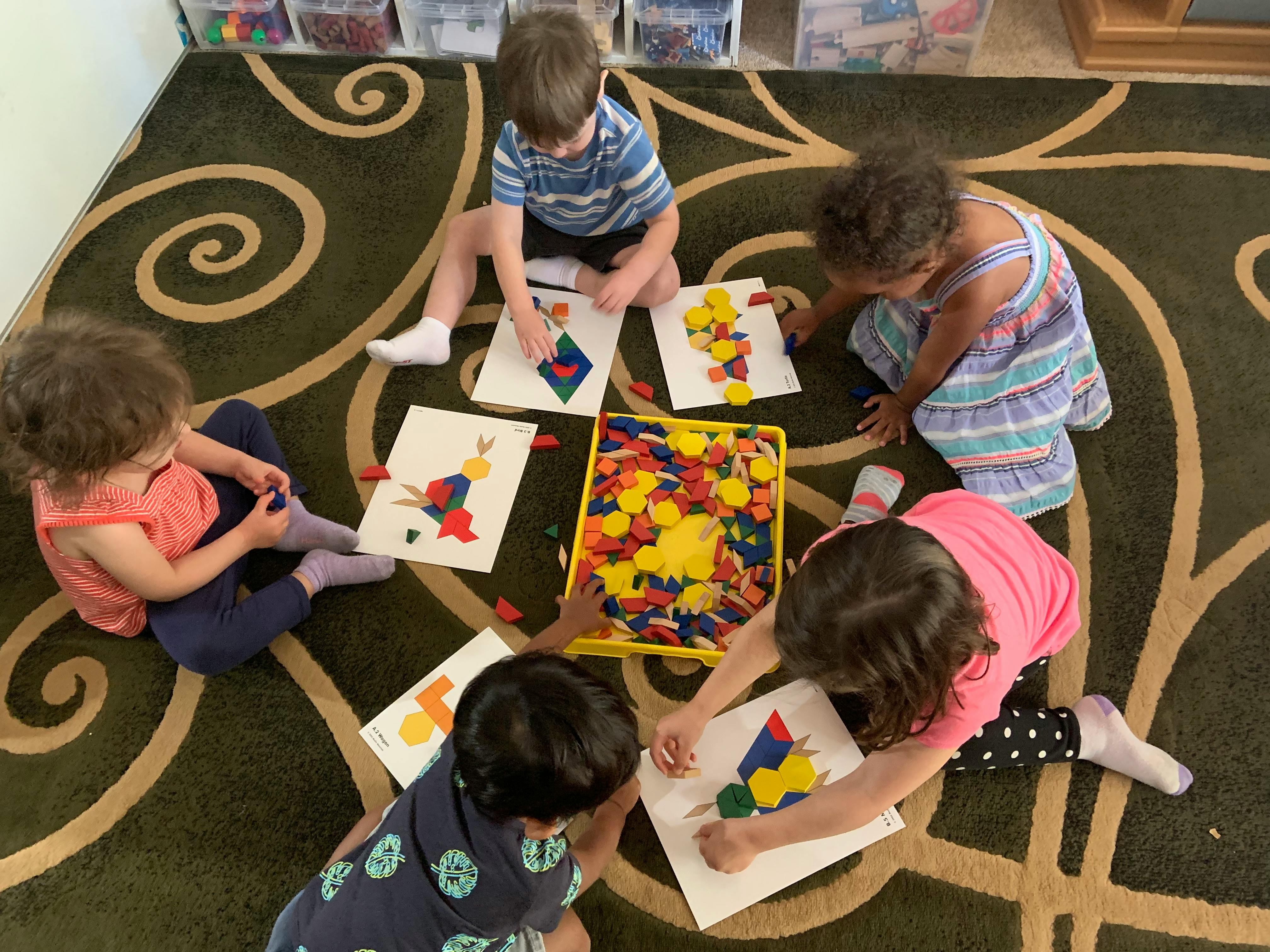 Children on a rug creating art with colorful shapes