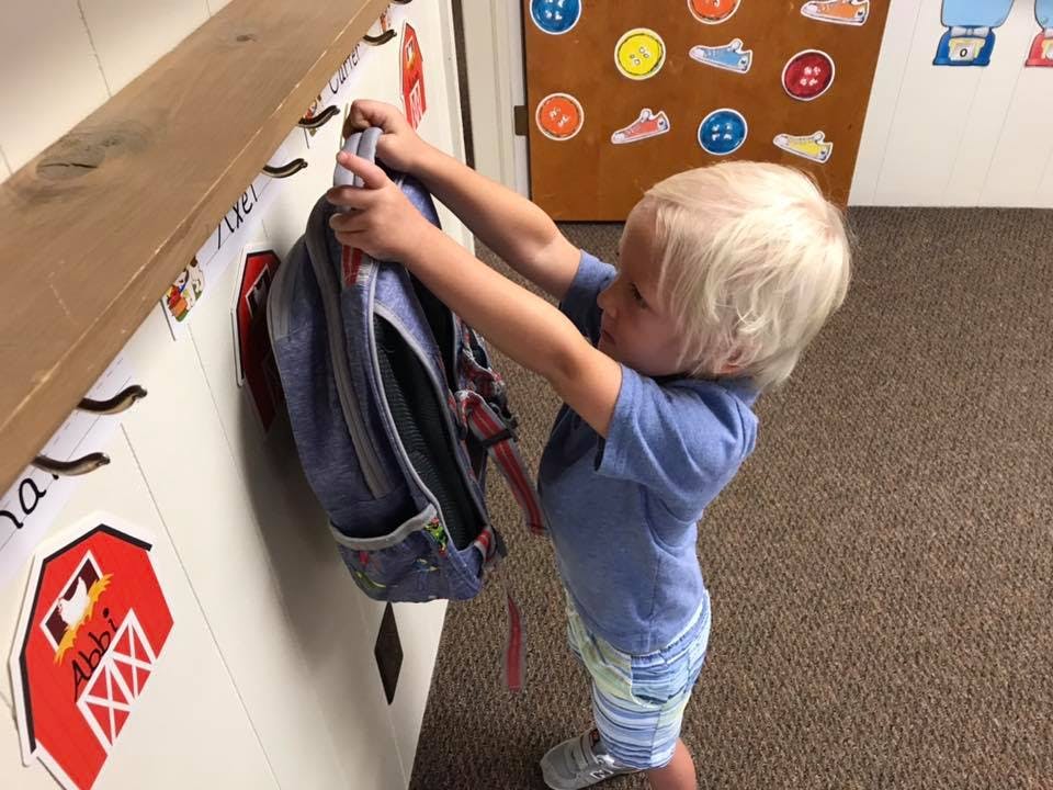 Child hanging a backpack on a hook
