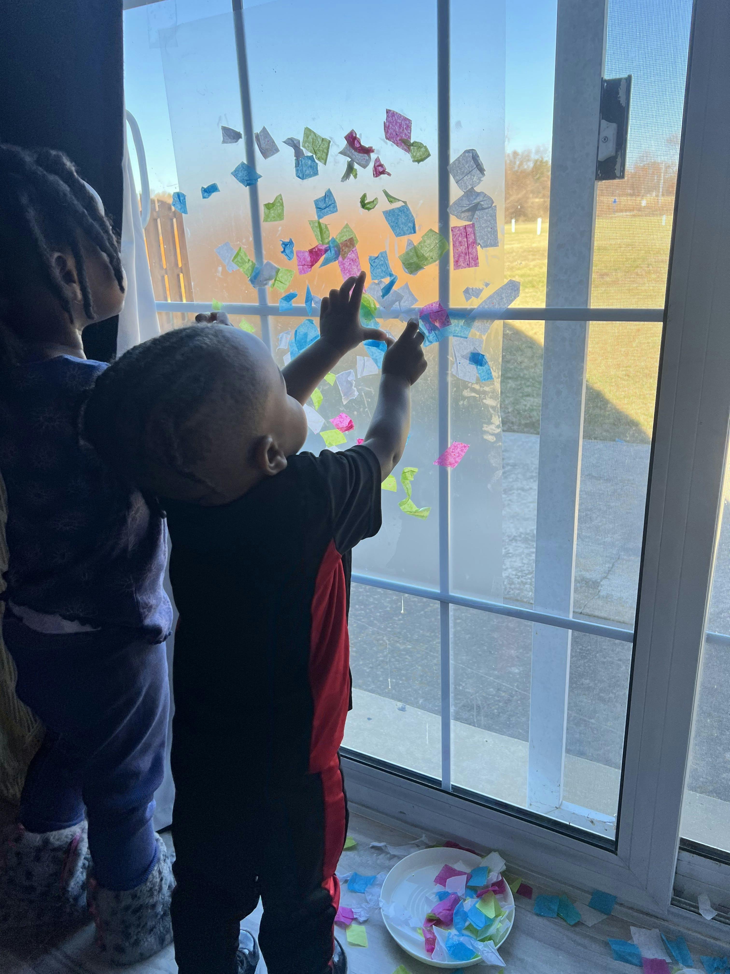 Child placing colorful paper squares on a window