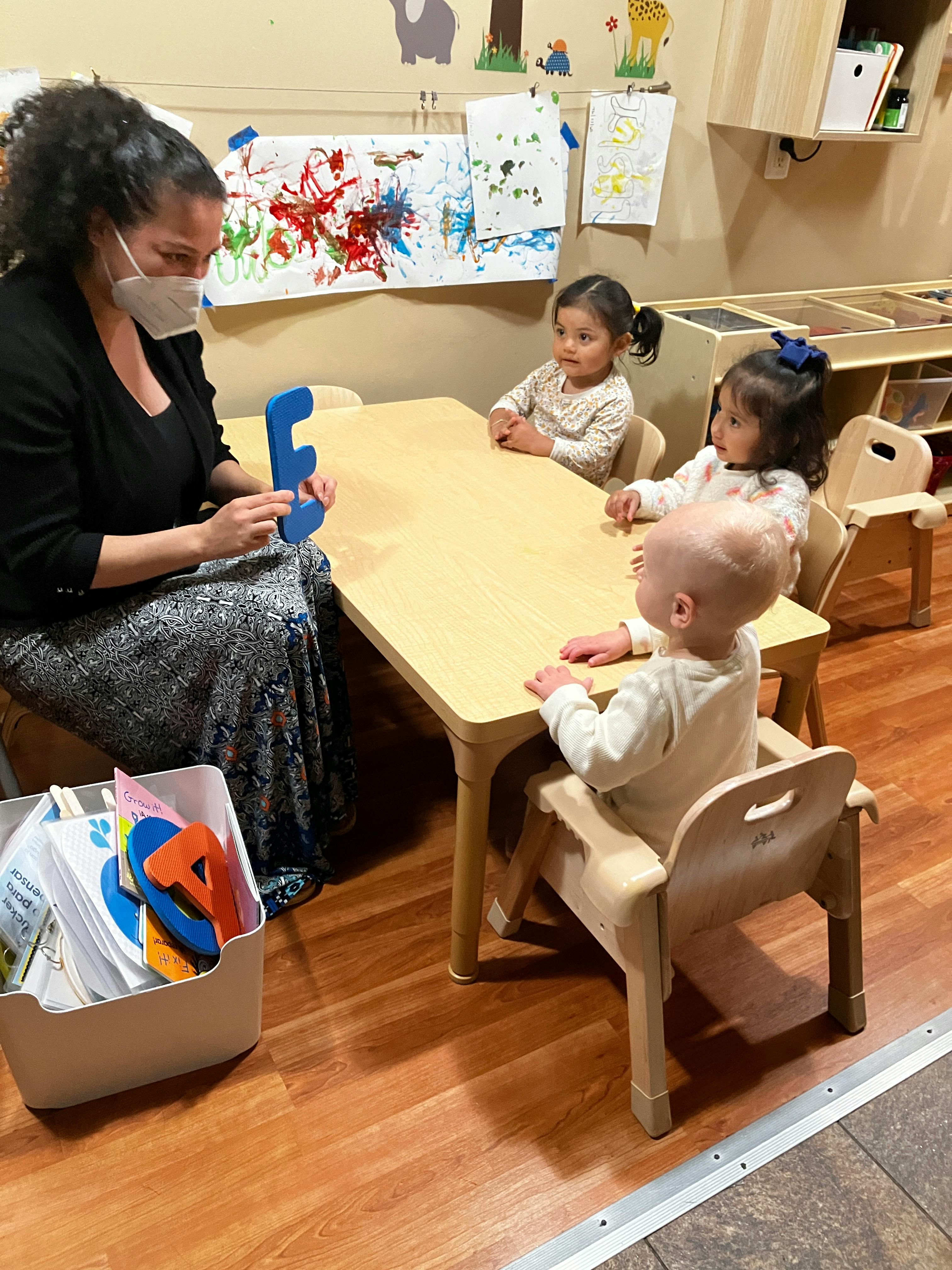 Person in mask holding a letter E with three children at a table