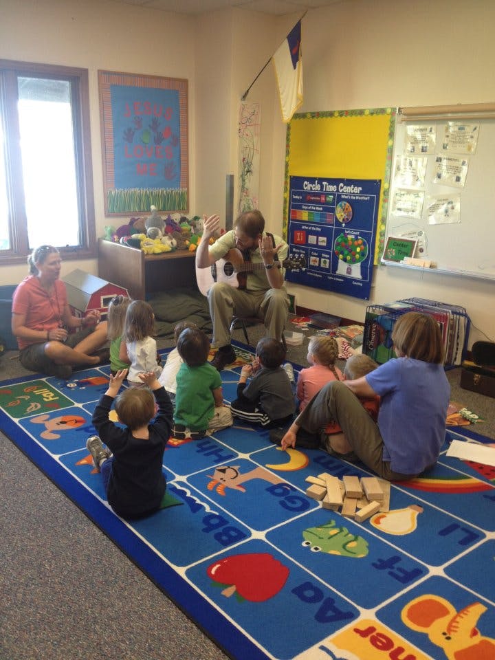 Adults and children sitting on a rug in a classroom