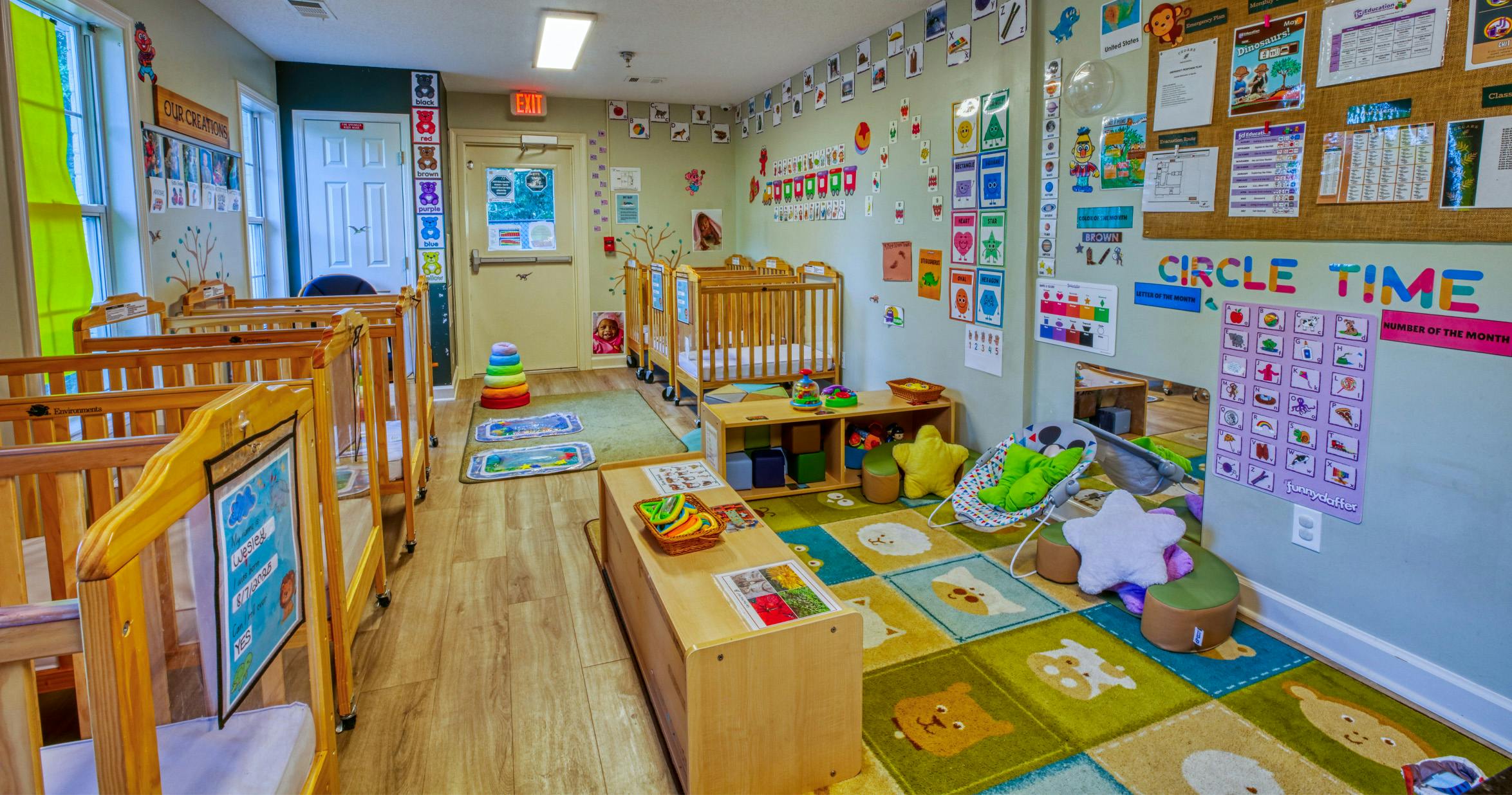 An infant daycare room with several wooden cribs and educational decorations