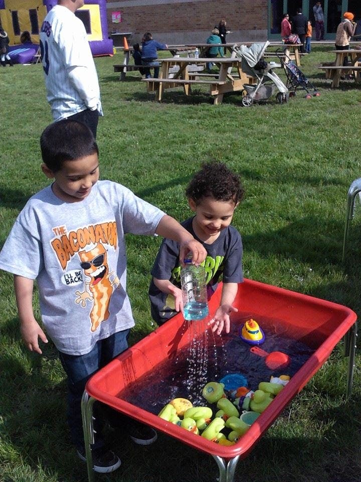 Two children playing with water in a red bin outdoors