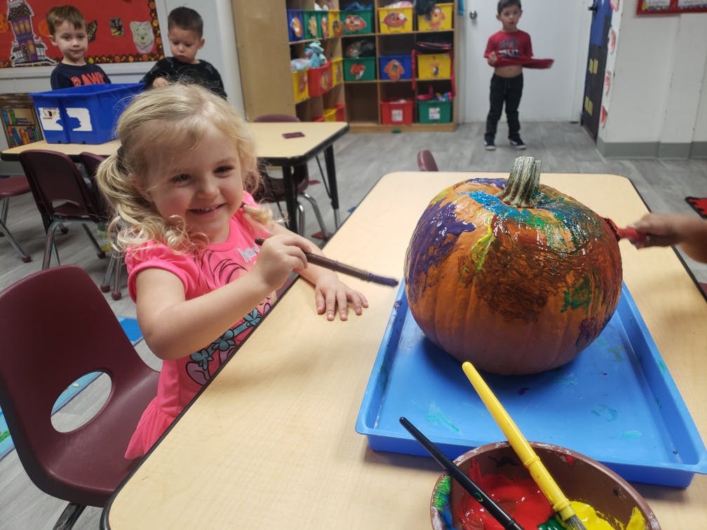 Child painting a pumpkin at a table