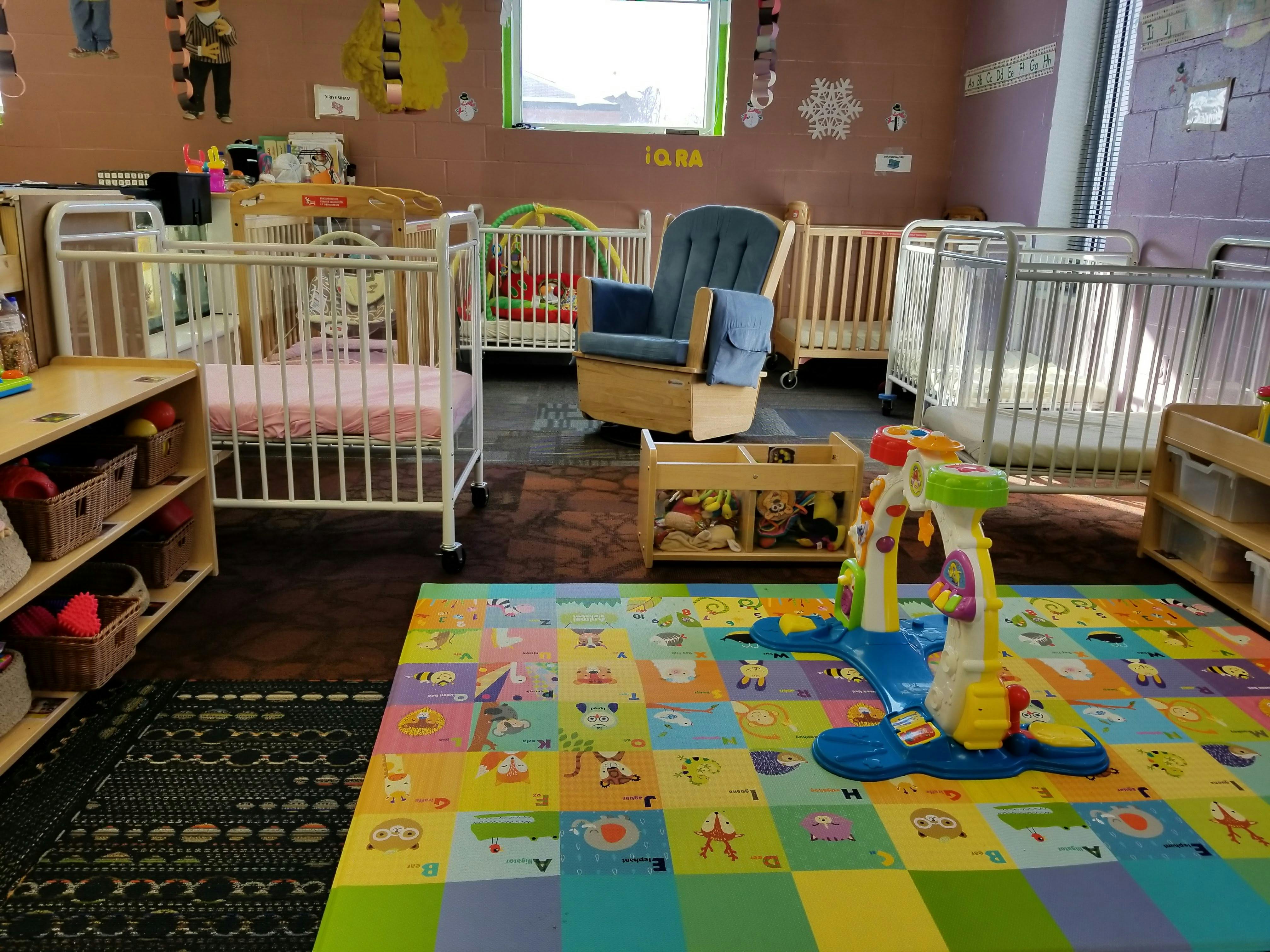 Nursery room with multiple cribs, a rocking chair, and a colorful play mat