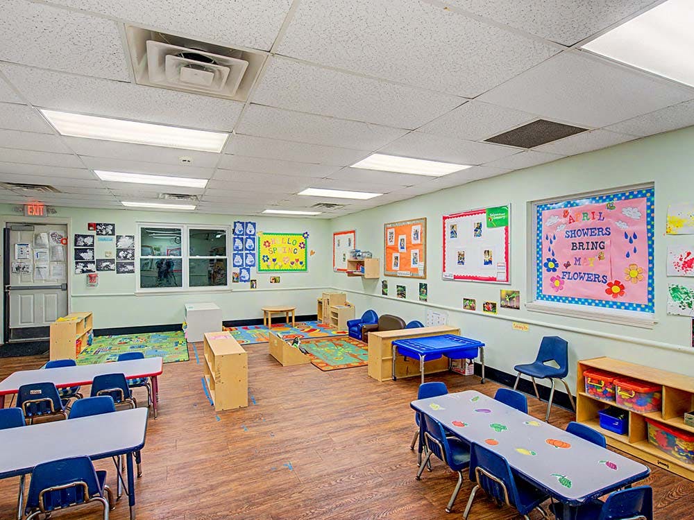 Empty children's classroom with small tables, chairs, and play areas