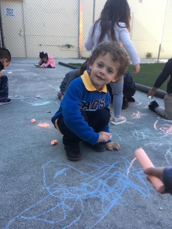 Child crouching and drawing with chalk on pavement