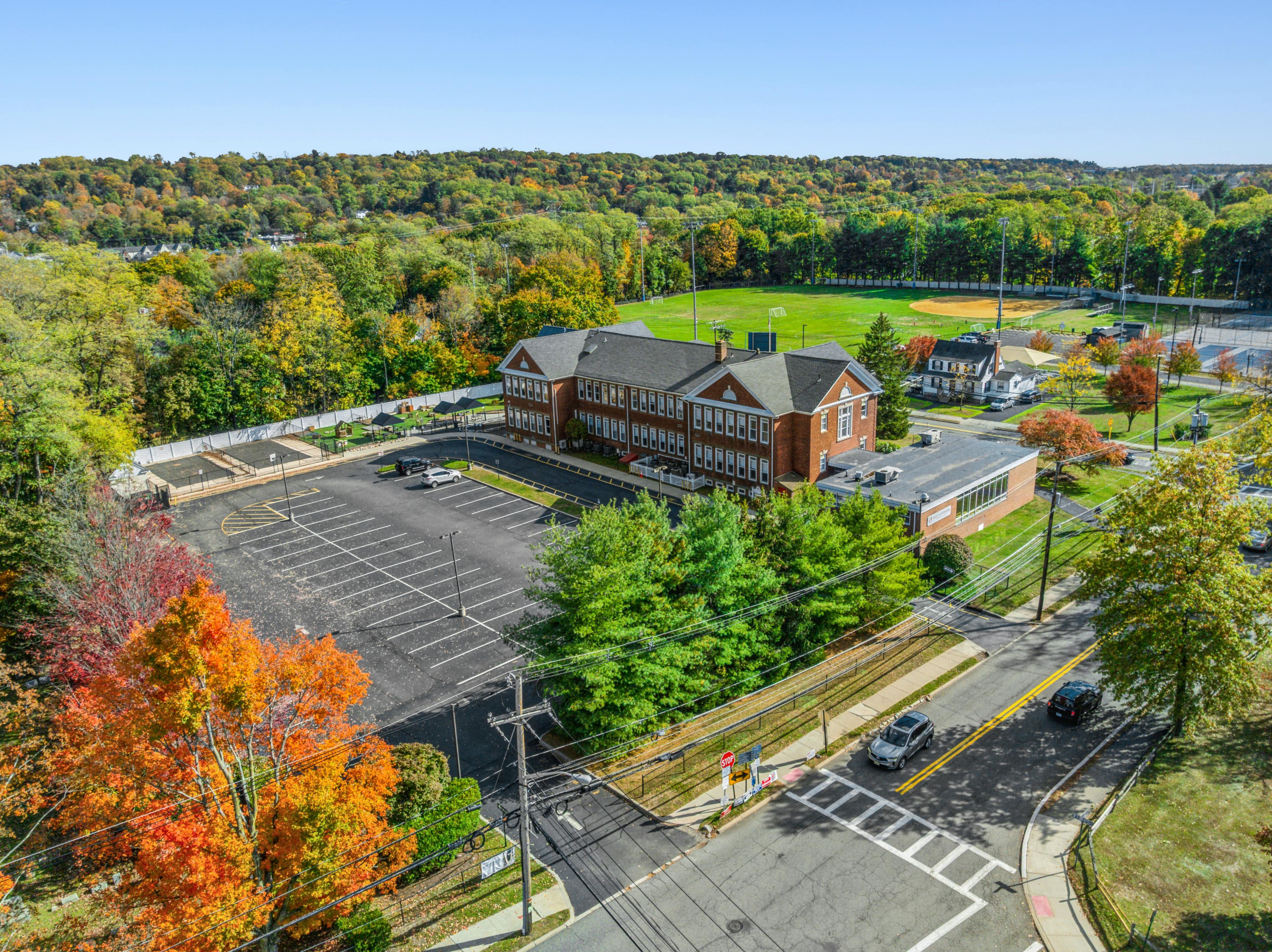 Aerial view of a brick school building with a parking lot and sports fields