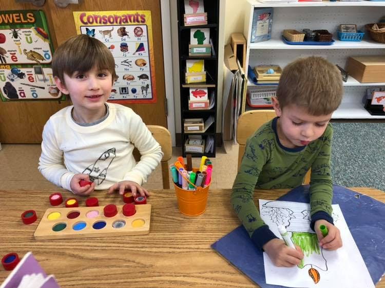 Two children at a table, one playing with a wooden puzzle, one coloring