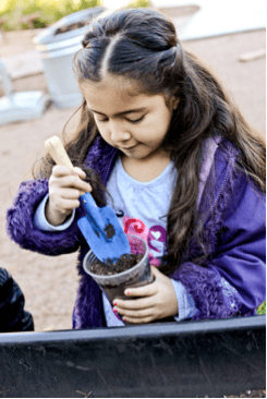 Child planting in a small pot with a trowel