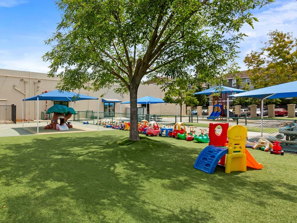 Outdoor playground with artificial turf, play structures, and small ride-on toys