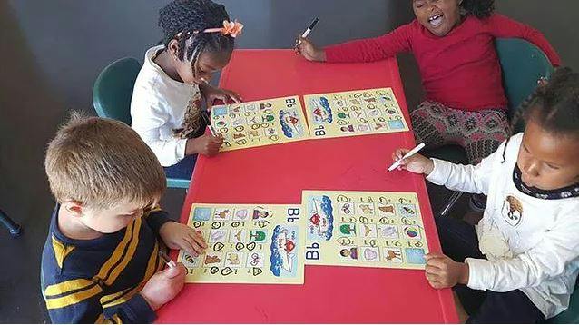 Four children sitting at a red table with activity sheets and coloring sheets