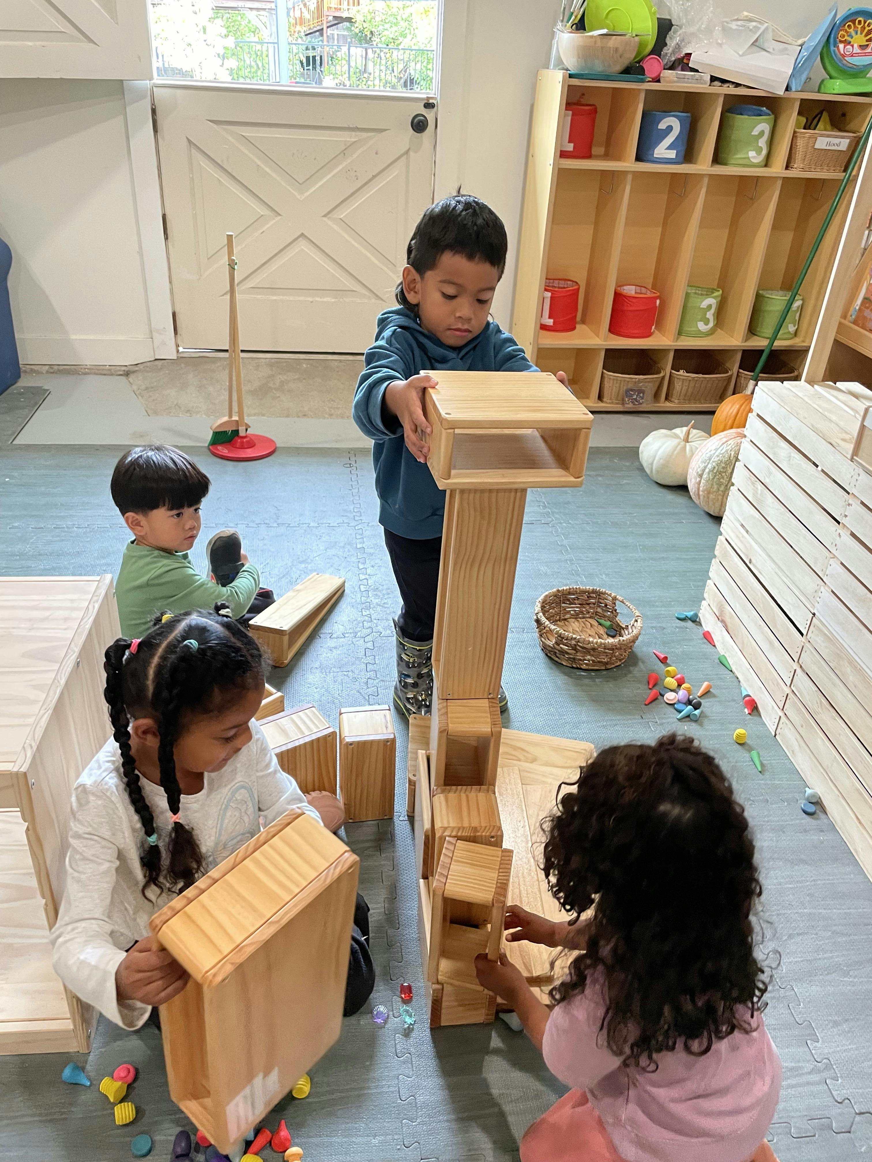 Three children playing with wooden blocks in a classroom