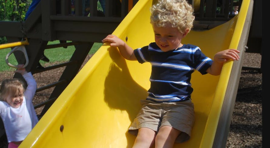 Child on a yellow slide with another child in the background