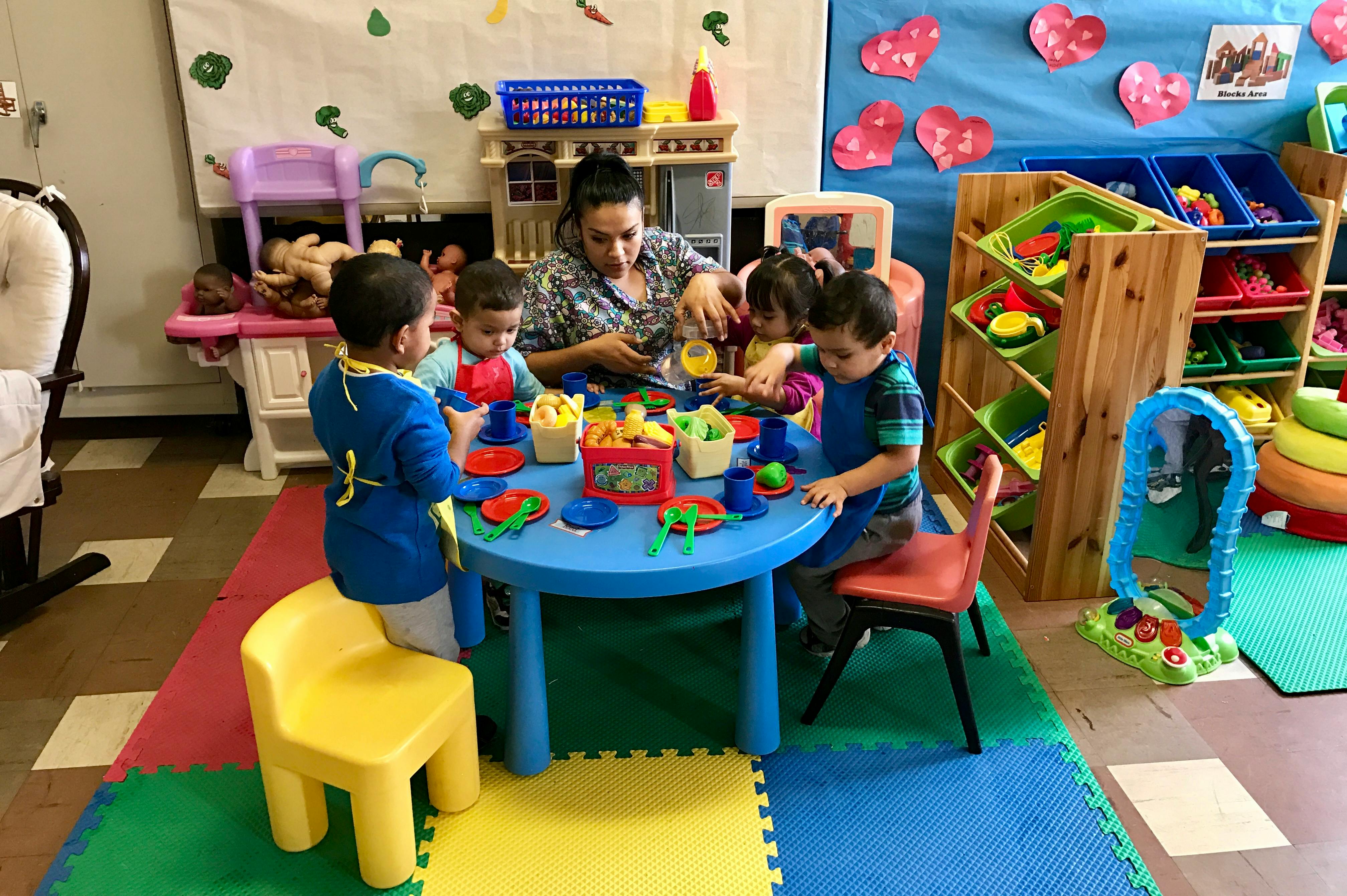 Adult and children playing with toys at a small blue table