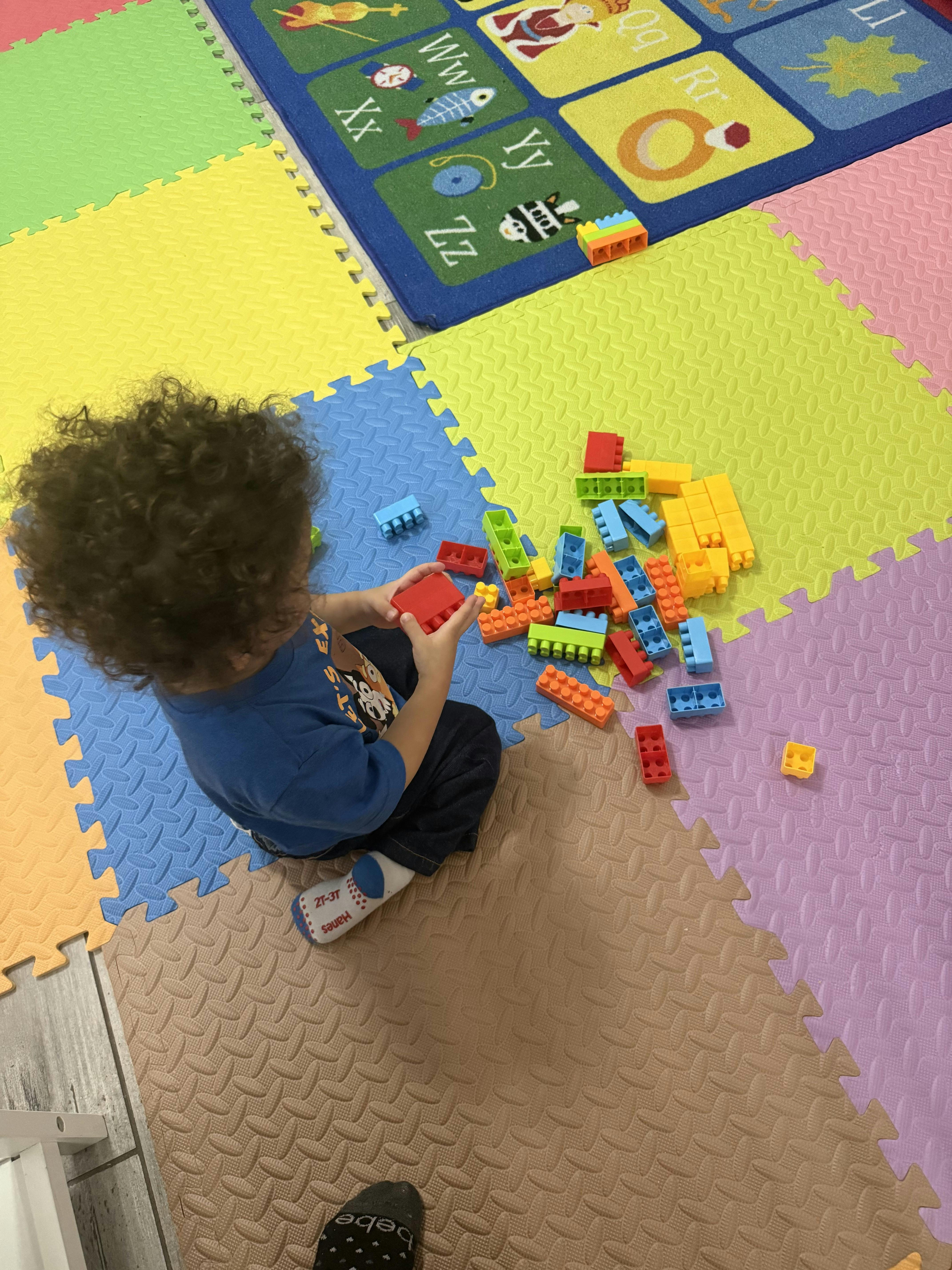 Child playing with plastic building blocks on a colorful foam floor mat