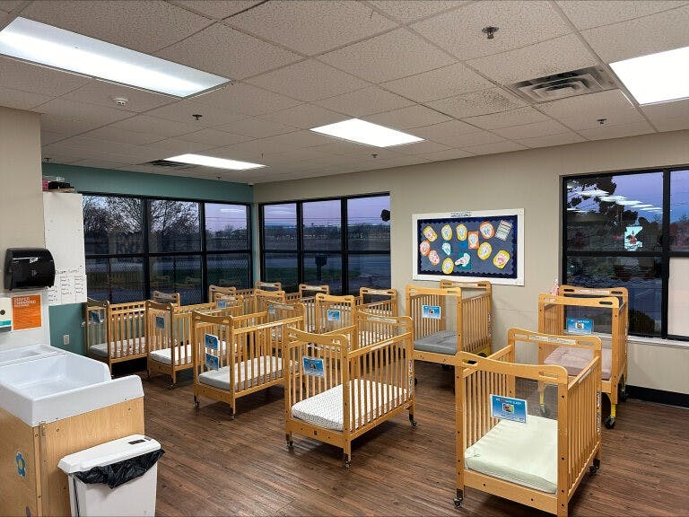 A room with multiple wooden cribs with mattresses and a changing station