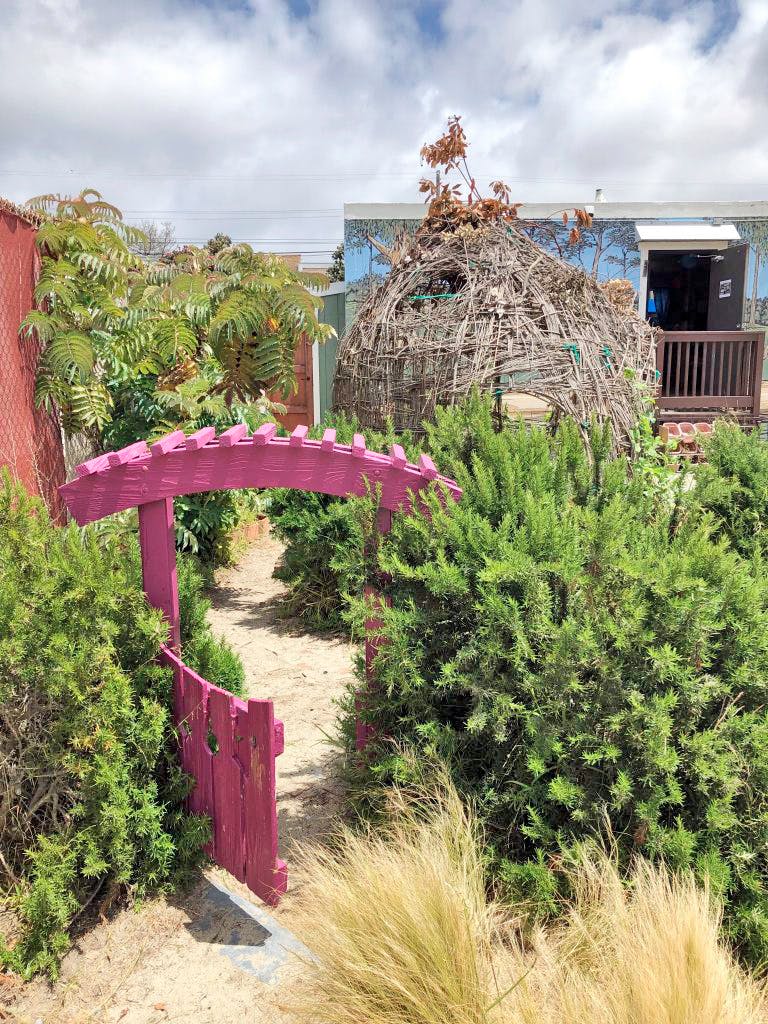 Pink garden gate and archway leading to a path through green bushes