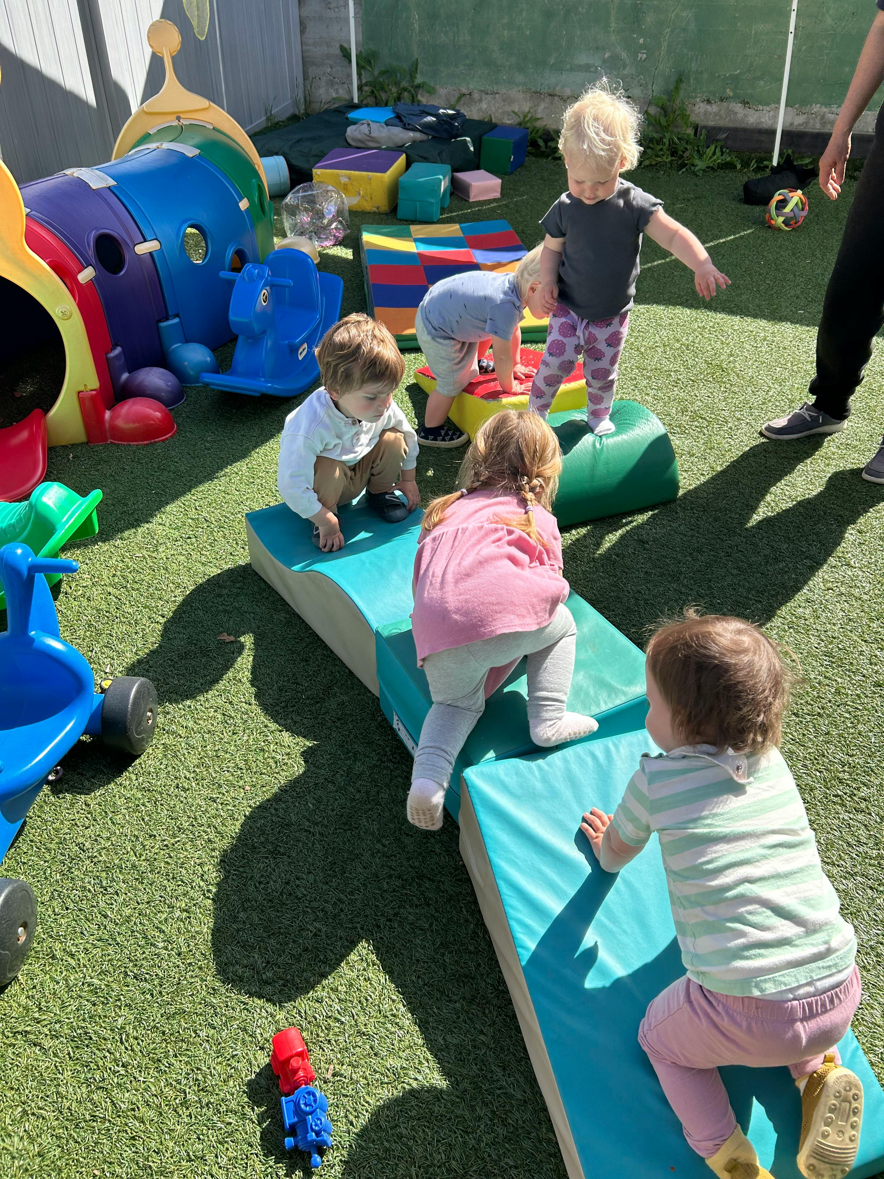Several children playing on soft mats and foam blocks outdoors