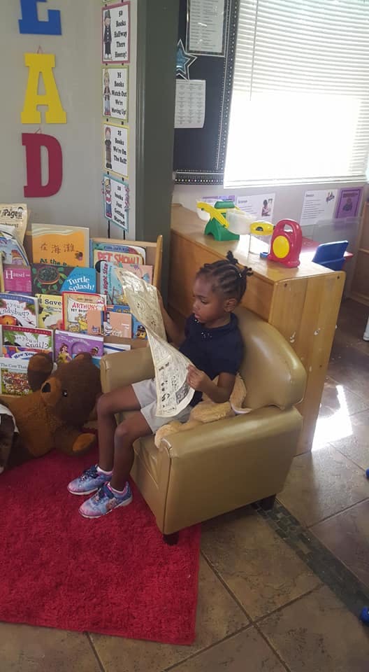 Child sitting in a chair reading a large piece of paper in a classroom