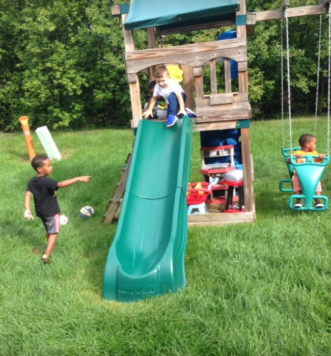 Three children playing on a backyard playset with a slide and swing