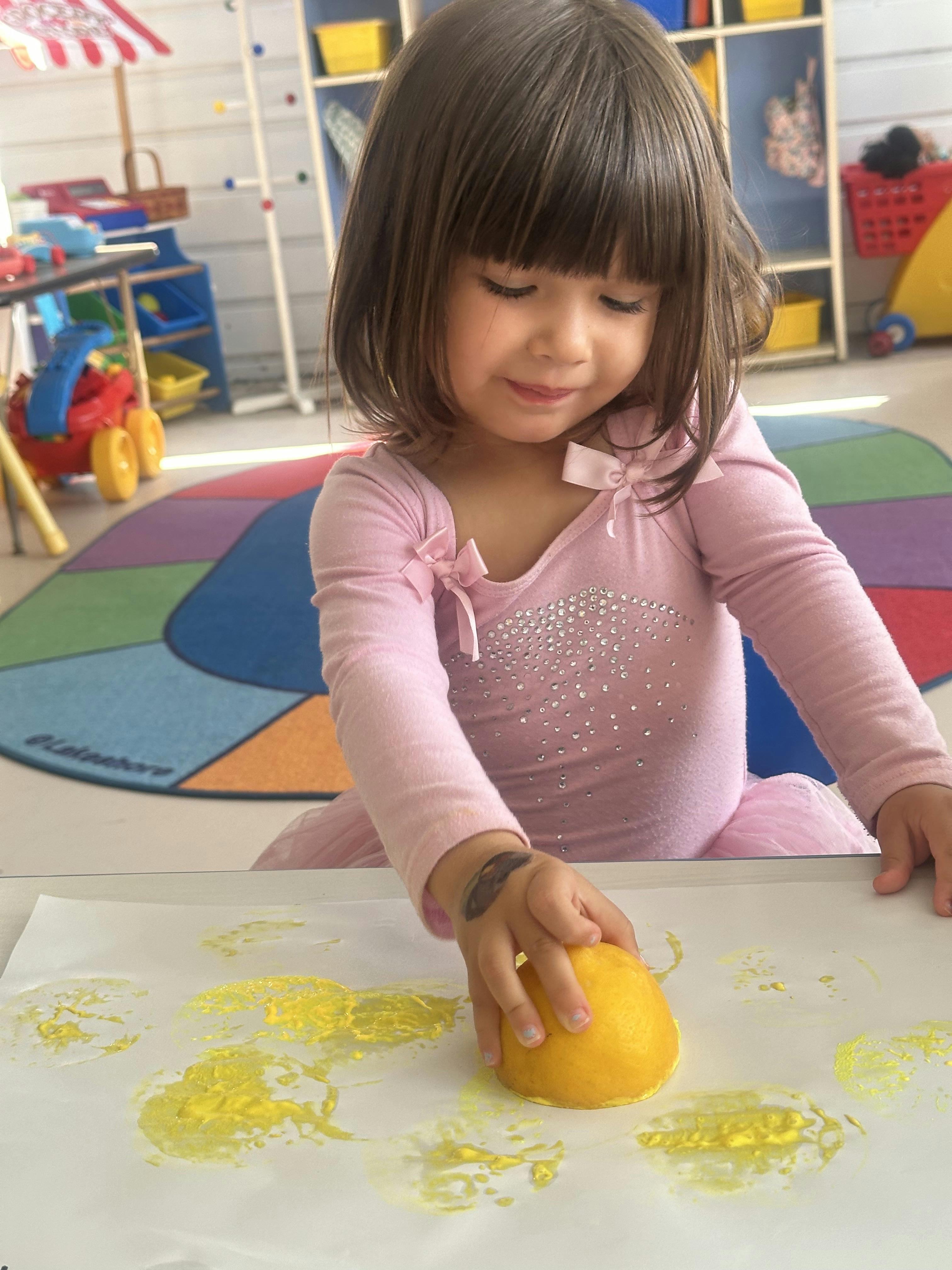 Child pressing half a lemon dipped in yellow paint onto white paper