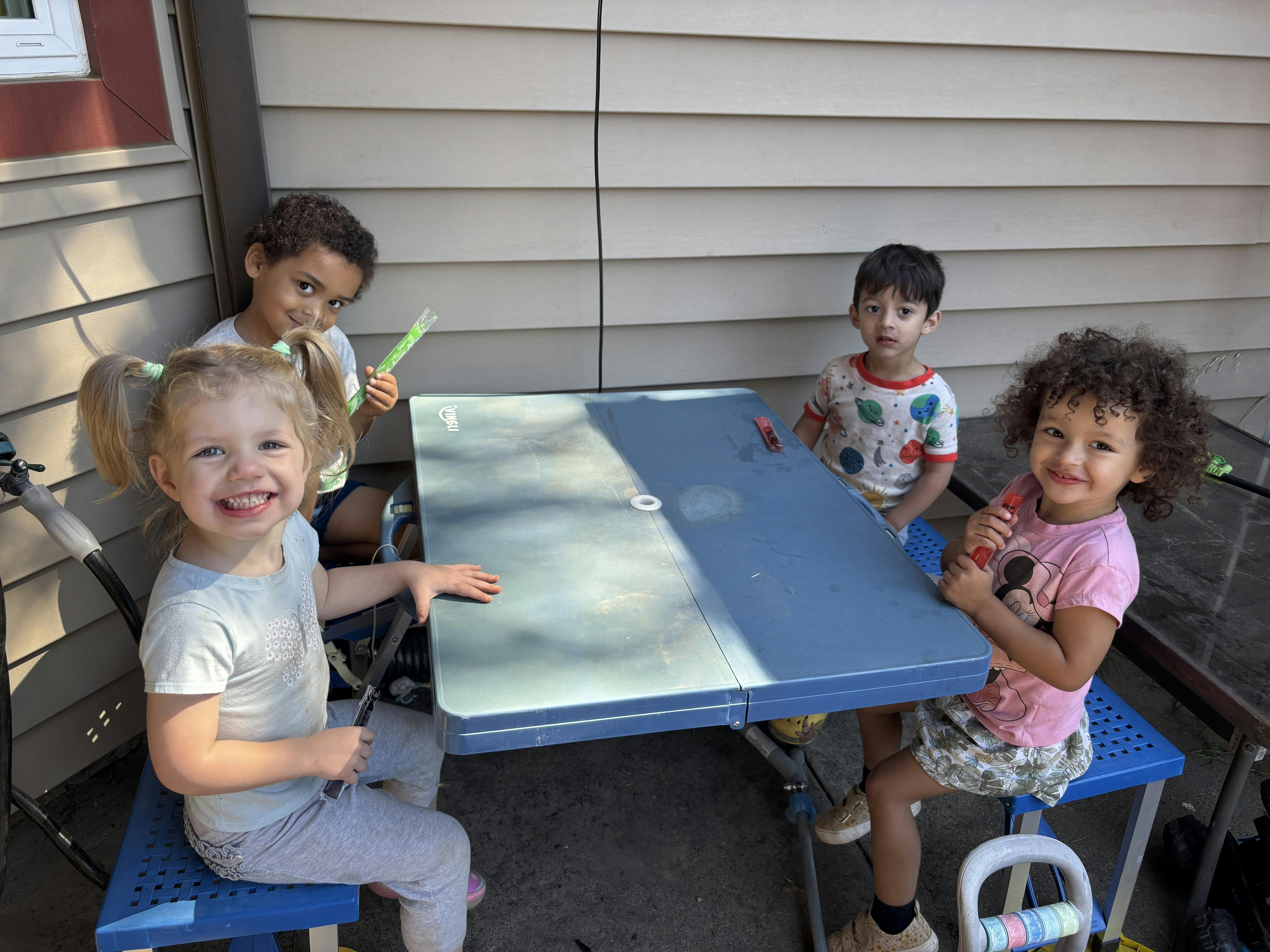 Four children sitting at a table outdoors