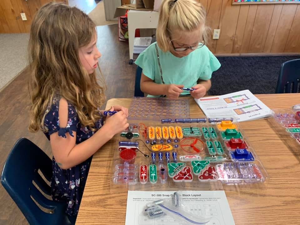 Two children at a table playing with a colorful electronics kit