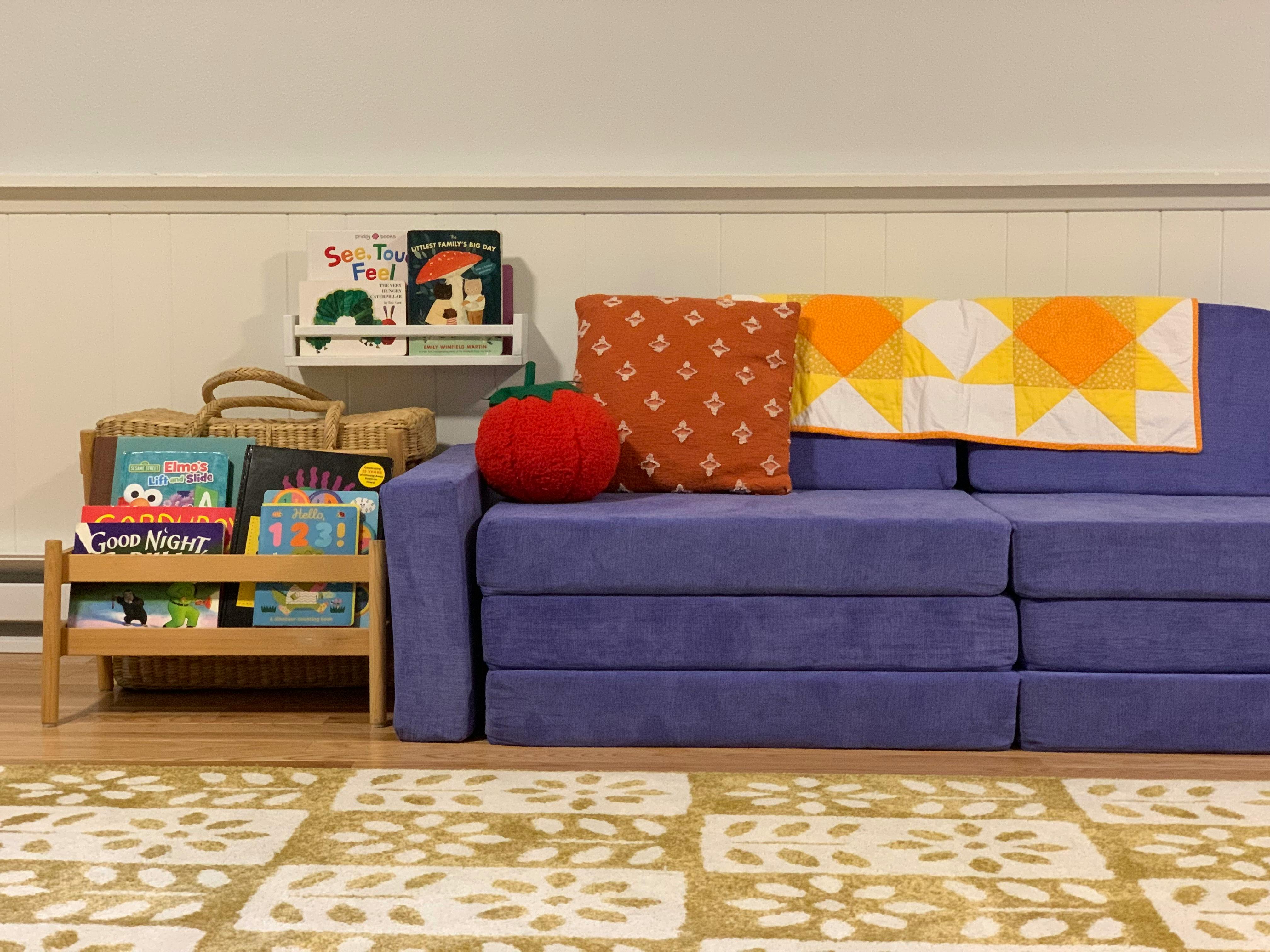 Purple modular sofa with pillows and a quilt next to a book display