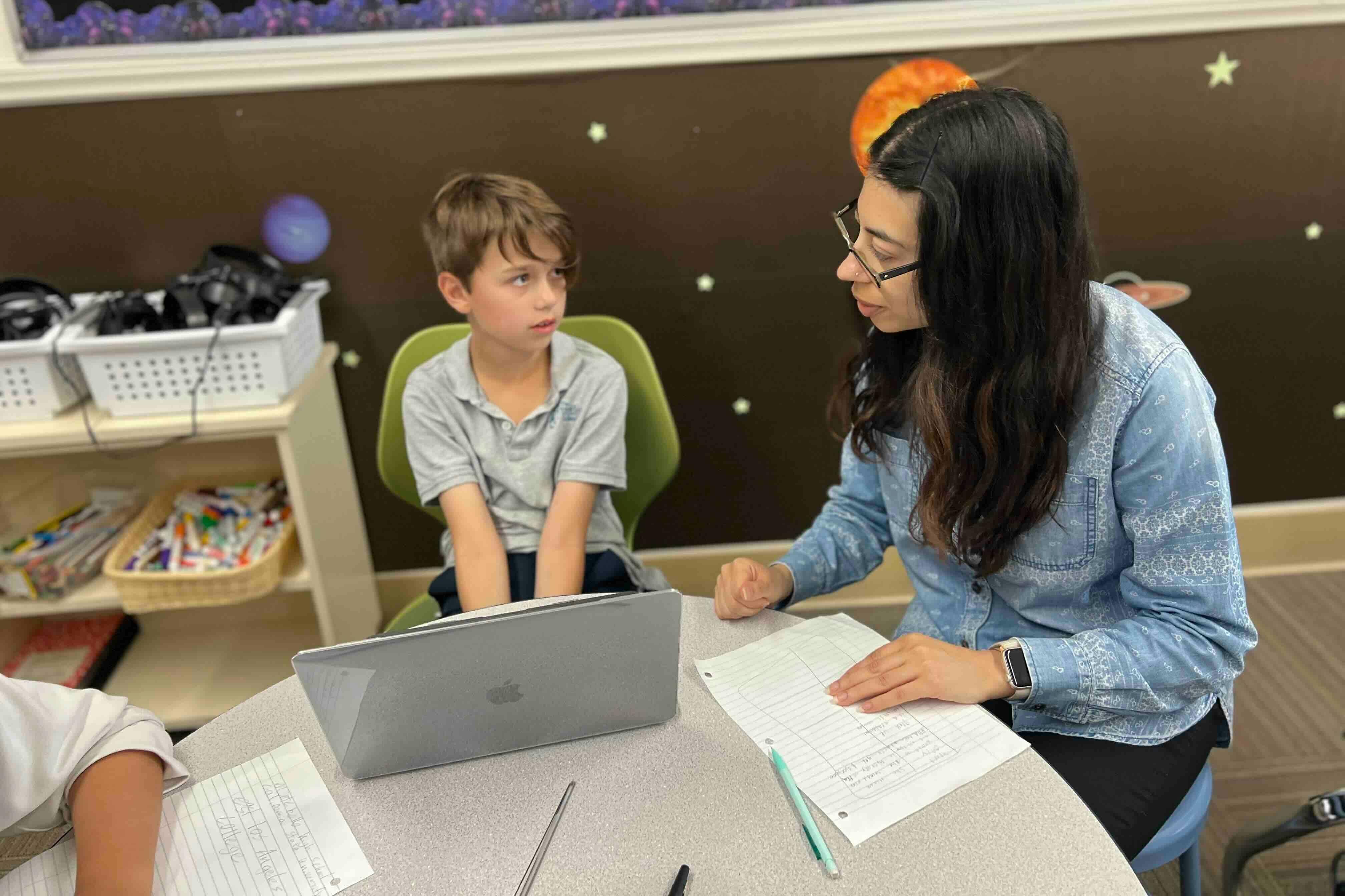 Adult and child in a classroom with a laptop and papers on a table